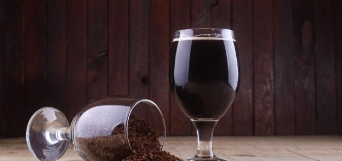 Glass of dark beer and some roasted malt over a wooden background