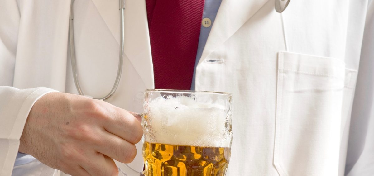 Male doctor is drinking light beer from the glass jug. One glass of beer a day concept.