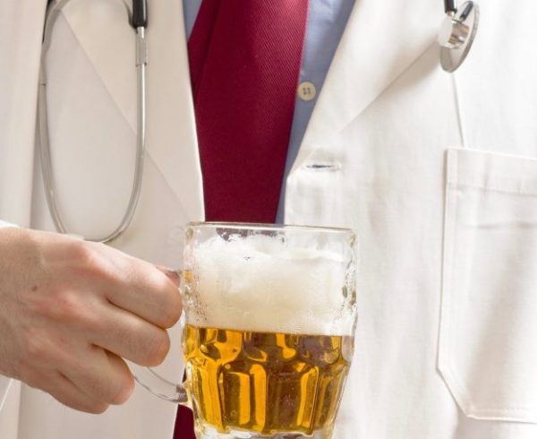 Male doctor is drinking light beer from the glass jug. One glass of beer a day concept.