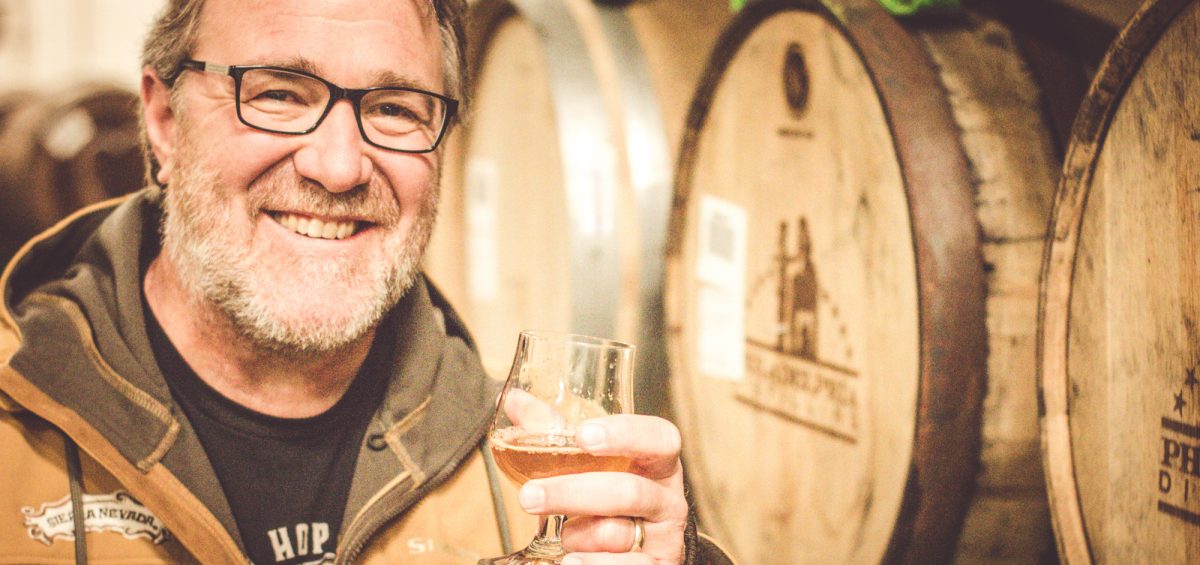 Terrence Sullivan from Sierra Nevada Brewing Company with glass in hand and barrels behind.