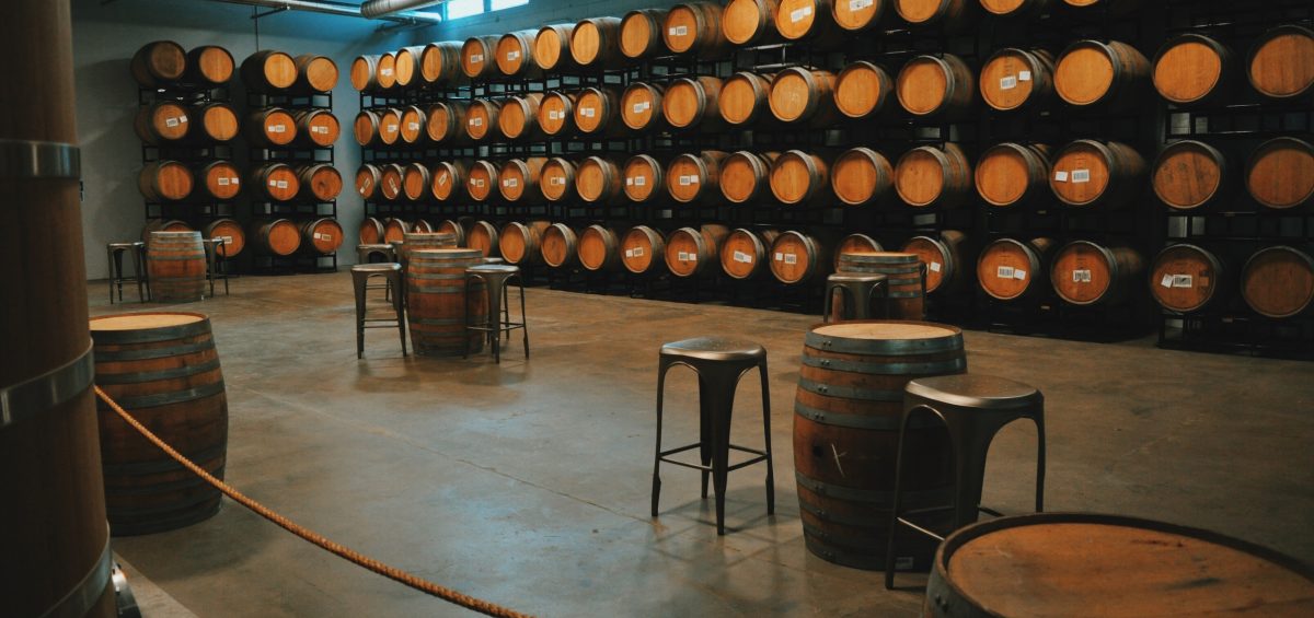 Barrel room with wall of wooden wine barrels and tables