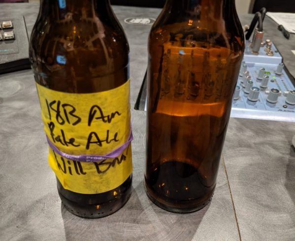 An American Pale Ale bottle and a Pilsner bottle are on the desk of the Dr. Homebrew podcast