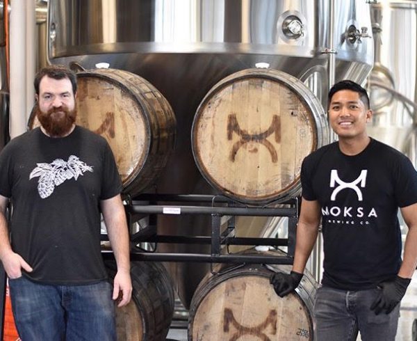 Brewers Derek Gallanosa and Cory Meyer in front of beer barrels at Moksa Brewing Company