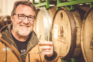 Terrence Sullivan from Sierra Nevada Brewing Company with glass in hand and barrels behind.