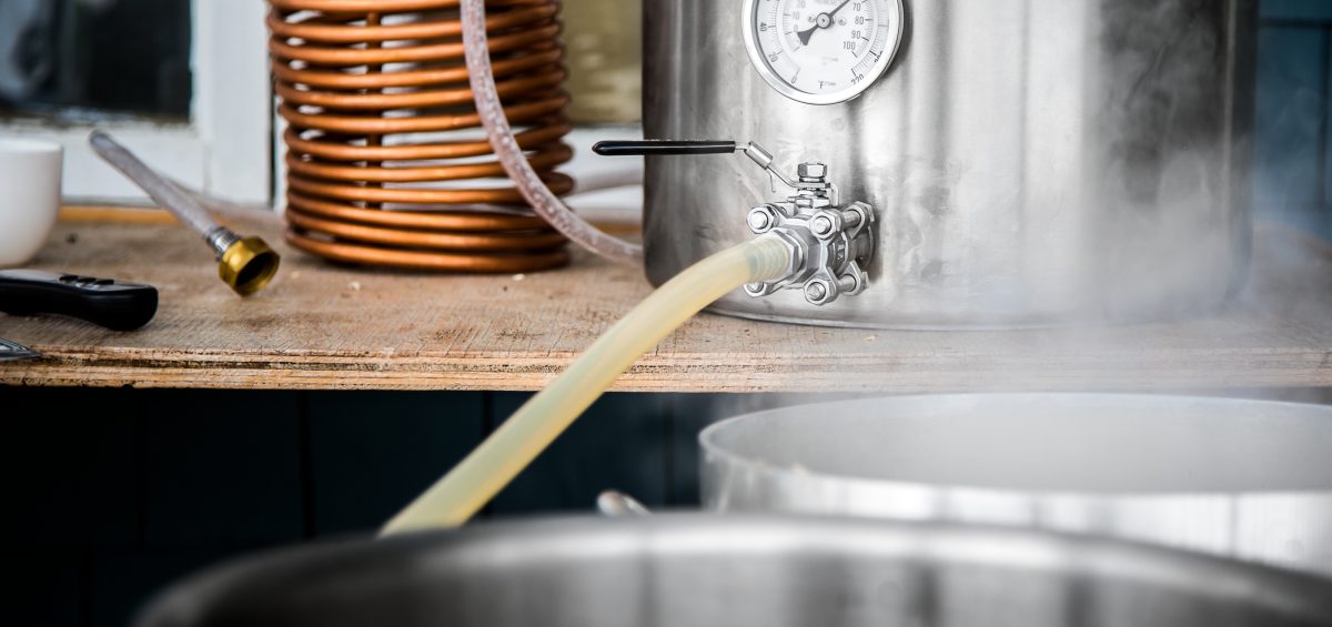Home Brewing Kit and Pouring Craft Beer Wort into the Boil Kettle with a Silicone Tube.