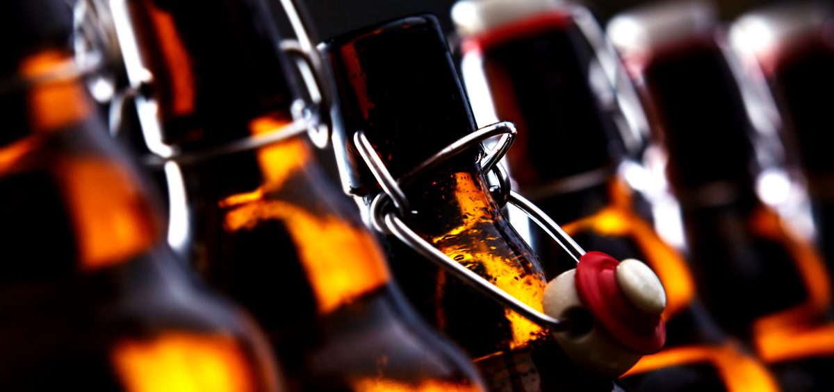 Row of beer bottles with stoppers glowing in the dark with selective focus to the stopper of an open bottle