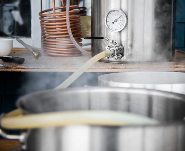 Home Brewing Kit and Pouring Craft Beer Wort into the Boil Kettle with a Silicone Tube.