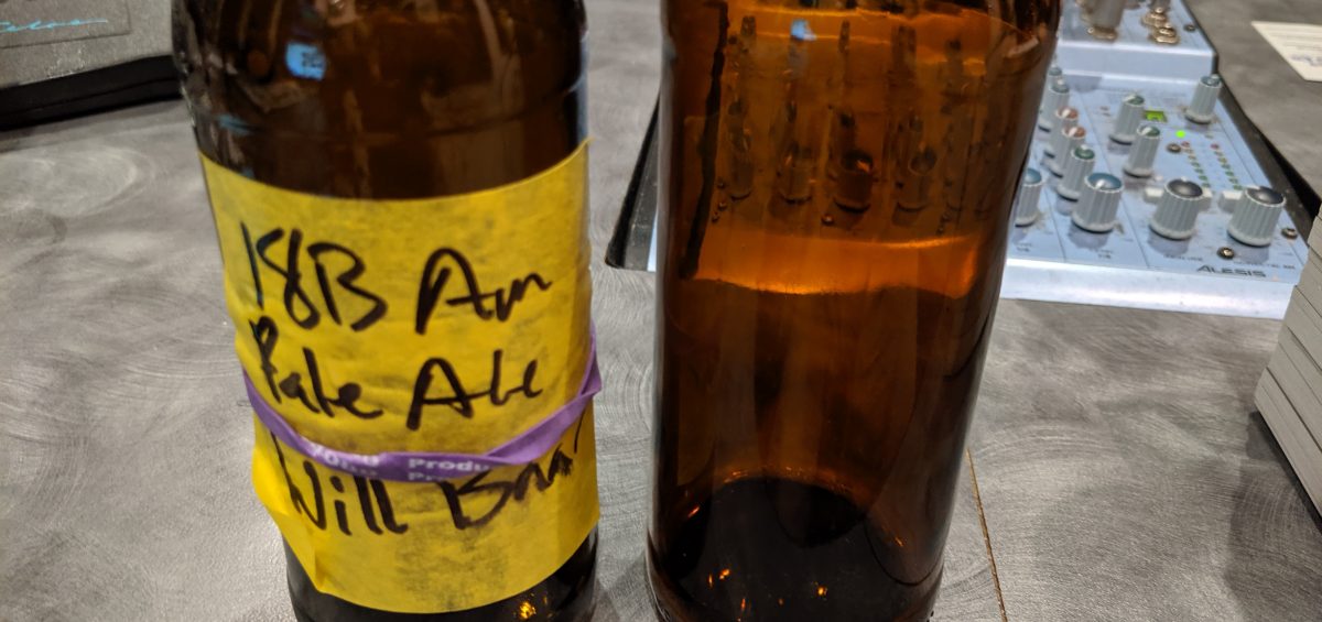 An American Pale Ale bottle and a Pilsner bottle are on the desk of the Dr. Homebrew podcast