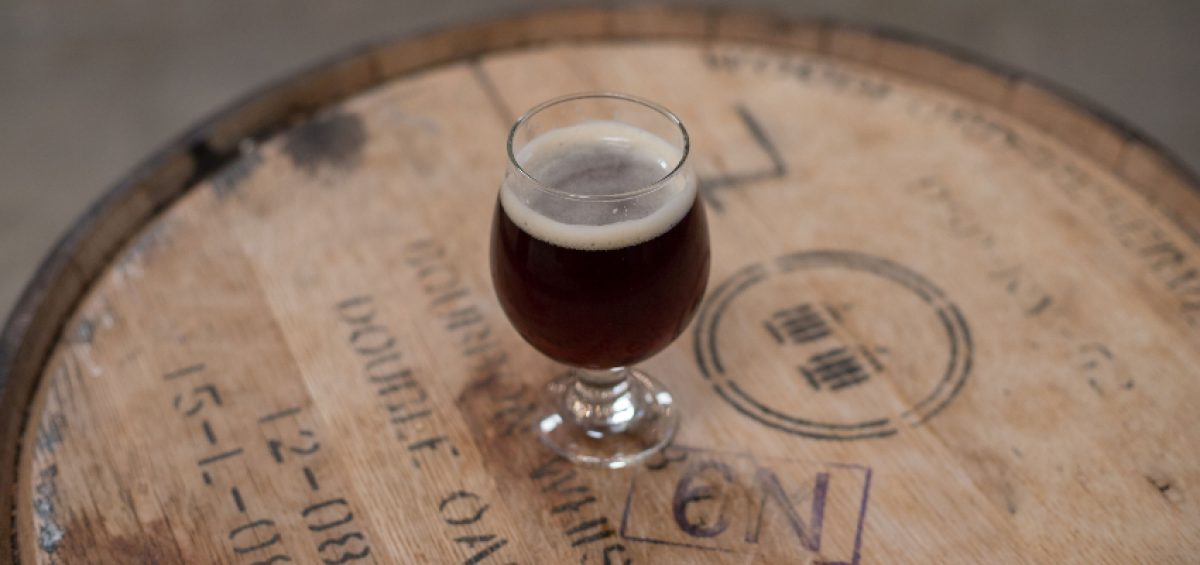 Barrel Aging Beer and beer glass on top of wooden barrel