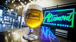Altamont Beer Works glass in front of neon sign