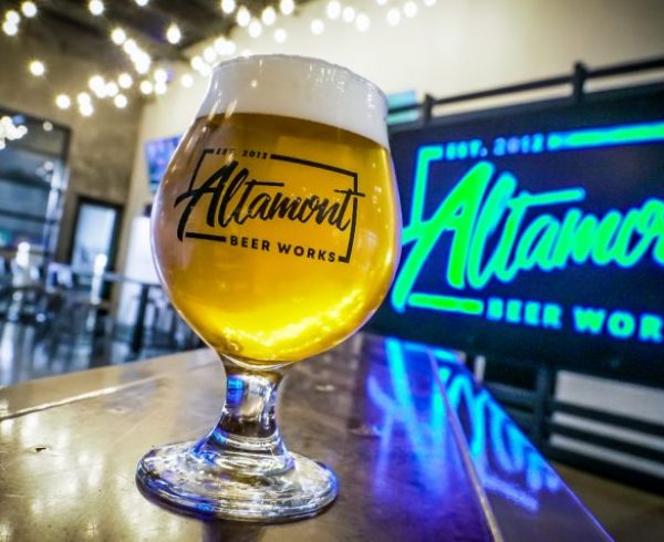 Altamont Beer Works glass in front of neon sign